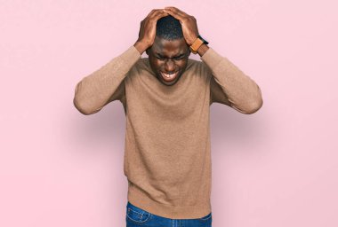Genç Afro-Amerikan adam günlük kazak giyiyor. Baş ağrısı çekiyor, çaresiz ve stresli. Çünkü acı ve migren ağrısı var. Eller başının üstünde.. 