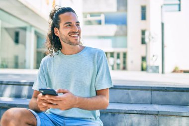 Genç İspanyol adam şehirde akıllı telefon kullanarak mutlu gülümsüyor..
