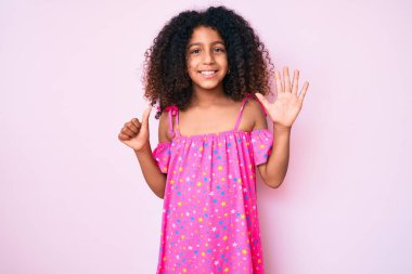 Kıvırcık saçlı Afrikalı çocuk gündelik elbisesini giyiyor ve altı numaralı parmaklarıyla işaret ederken kendinden emin ve mutlu bir şekilde gülümsüyor.. 