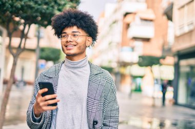 Genç Afrikalı Amerikalı iş adamı şehirde akıllı telefon kullanarak mutlu bir şekilde gülümsüyor..