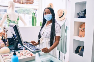Giyim mağazasında çalışan, tıbbi maske takan Afro-Amerikan bir kadın.