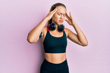 Güzel sarışın kadın spor kıyafetleri giyiyor ve kulaklık kullanıyor. Başı ağrıyor çünkü stres altında. migren ağrısı. 
