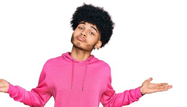 Afro saçlı, pembemsi bir kazak giyen, elleri ve kolları havada, kafası karışık, Afro-Amerikan bir genç. şüphe kavramı. 