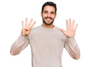 Gündelik kıyafetler giyen genç İspanyol adam dokuz numarayı gösterip işaret ederken kendinden emin ve mutlu bir şekilde gülümsüyor.. 