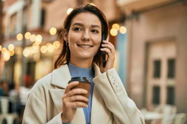 Genç İspanyol kadın akıllı telefondan konuşuyor ve şehirde kahve içiyor..