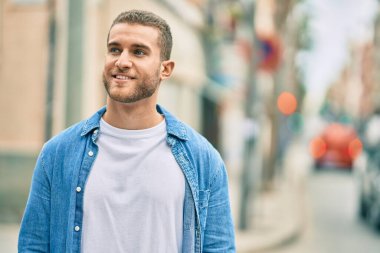 Genç beyaz adam gülümseyerek şehirde mutlu mesut duruyor..