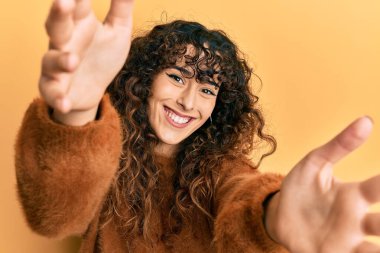 Gündelik giysiler giymiş genç İspanyol kız kameraya sarılmak için kollarını açmış gülümseyerek bakıyor. Mutluluğu kucaklayan neşeli bir ifade.. 