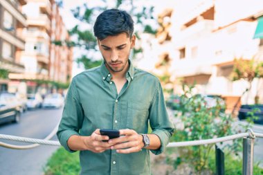 Şehirde akıllı telefon kullanan, ciddi bir suratı olan genç bir latin..