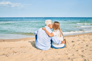 Orta yaşlı İspanyol sarılıp kumsalda oturuyor.