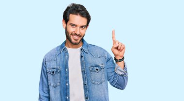 Gündelik kıyafetler giyen genç İspanyol adam başarılı bir fikirle işaret ediyor. Heyecanlı ve mutlu. Bir numara.. 