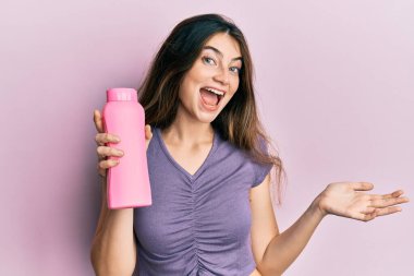 Genç beyaz kadın elinde şampuan şişesi tutarak başarıyı mutlu bir gülümsemeyle ve kazanan yüz ifadesiyle kutluyor. 