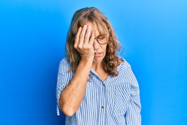 Orta yaşlı sarışın kadın gündelik kıyafetler giyiyor ve gözlük takıyor. Yarı yüz, yarı göz, yarı ağız ve yarı el ile esnemekten yorgun düşüyor. Yüzüm acıyor.. 