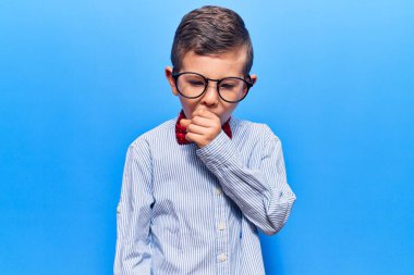 İnek papyonu takan ve gözlük takan sevimli sarışın çocuk kendini iyi hissetmiyor ve soğuk algınlığı veya bronşitin belirtisi olarak öksürüyor. sağlık hizmeti kavramı. 