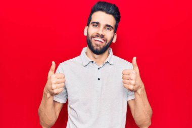 Sakallı, sıradan polo başarısı işareti takan, elinde olumlu bir jest yapan, gülümseyen ve mutlu genç yakışıklı bir adam. Neşeli ifade ve kazanan jest. 