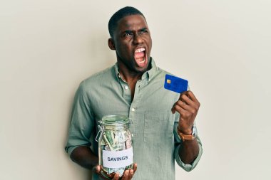 Genç Afro-Amerikalı adam elinde kredi kartı ve kavanoz dolusu dolar tutuyordu kızgın ve öfkeli çığlıklar atıyordu öfkeyle bağırıyordu. öfke ve agresif konsept. 