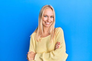 Sıradan kıyafetler giyen, kollarını kavuşturup kameraya bakan mutlu yüzlü genç sarışın kız. pozitif kişi. 