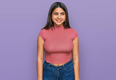 Gündelik tişört giyen genç İspanyol kız yüzünde gülümsemeyle yan yana bakıyor, doğal bir ifade. Kendinden emin gülen. 