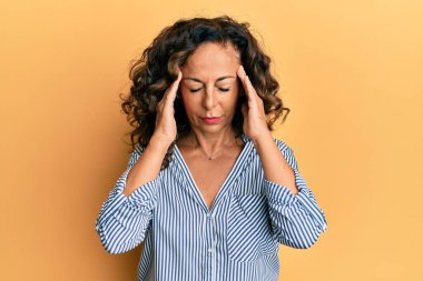 Orta yaşlı İspanyol kadın stres yüzünden elleri başının üstünde gündelik kıyafetler giyiyor. migren ağrısı. 