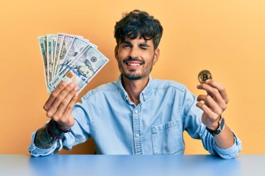 Dolarları tutan genç İspanyol adam ve Bitcoin kameraya seksi bir ifadeyle bakıyor, neşeli ve mutlu bir yüz.. 