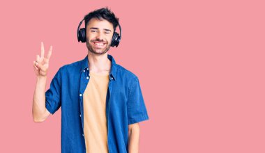 Genç İspanyol adam müzik dinliyor kulaklık takıyor kameraya gülümseyen bir gülümsemeyle zafer işareti yapıyor. İki numara.. 