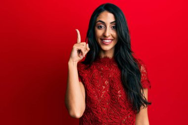 Kırmızı arka planda zarif elbiseler giyen güzel İspanyol kadın başarılı bir fikri işaret ediyor. Heyecanlı ve mutlu. Bir numara.. 