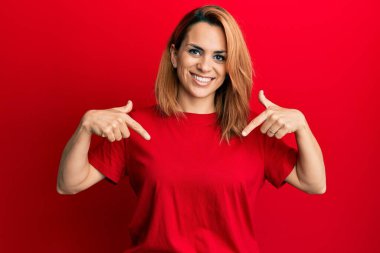 Latin kökenli genç bir kadın, gündelik kırmızı tişört giyiyor. Kendine güveni tam görünüyor. Kendini gururlu ve mutlu bir şekilde gösteriyor.. 
