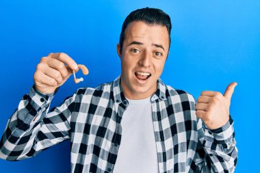 Elinde tıbbi işitme cihazı olan yakışıklı genç adam baş parmağını yana kaldırmış, ağzı açık gülümsüyor. 