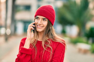 Kış tarzı giyinen genç İspanyol kadın şehirde akıllı telefondan konuşuyor..