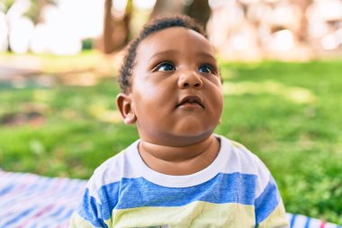 Sevimli Afro-Amerikan çocuk parkta çimlerin üzerinde oturuyor..