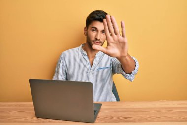 Ofiste dizüstü bilgisayarı açık çalışan yakışıklı bir adam dur işareti yapıyor ciddi ve kendinden emin bir ifadeyle savunma hareketi yapıyor. 