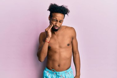 Sakallı, mayo giyen, diş ağrısı ya da diş hastalığından dolayı acı dolu bir ifadeyle dudaklarına dokunan Afrikalı genç bir Amerikalı. dişçi 