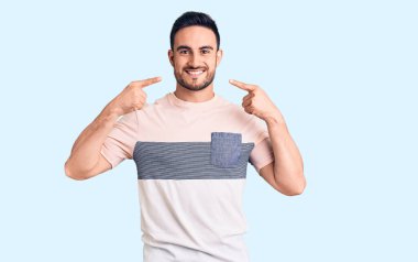 Gündelik kıyafetler giyen, neşeli gülümseyen, parmaklarıyla ve ağzıyla işaret eden genç yakışıklı bir adam. diş sağlığı kavramı. 