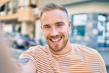 Genç İrlandalı gülümseyen adam şehrin caddesindeki kameranın önünde selfie çekerken mutlu oluyor..