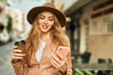Genç sarışın kız akıllı telefon kullanıyor ve şehirde kahve içiyor..