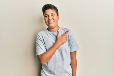 Gündelik gri tişört giyen genç İspanyol çocuk. Yüzünde mutlu ve doğal bir ifadeyle, elleri ve parmaklarıyla yüzünü gösteren bir gülümseme var. 