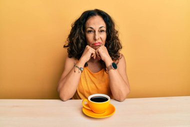 Güzel, orta yaşlı bir kadın bir fincan kahve içerken kollarını kavuşturup depresyondan sıkılmış ve yorgun görünüyor.. 