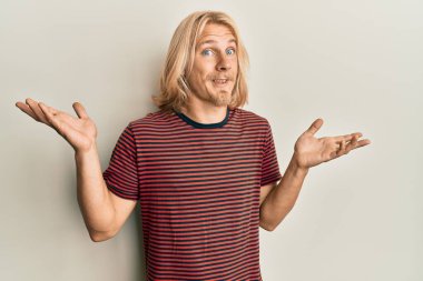 Kafkasyalı, uzun saçlı, sıradan çizgili tişört giyen, kafası karışık, kolları açık, hiçbir fikri olmayan, şüpheli bir yüzü olan bir genç.. 