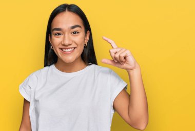 Genç Asyalı kadın, günlük beyaz tişörtler giyip gülümsüyor ve el hareketleriyle küçük boy işaretler yapıyor, parmakları görünüyor ve kameraya bakıyor. ölçüm kavramı. 