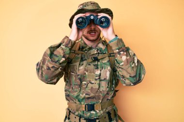 Kafkasyalı genç adam kamuflaj üniforması giyiyor. Şok suratlı dürbün kullanıyor. Şüpheci ve alaycı görünüyor. 