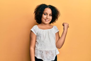 Afro saçlı, sıradan kıyafetler giyen mutlu yüzüyle gülümseyen ve baş parmağıyla yüzünü gösteren küçük bir kız.. 