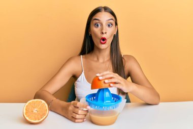 Masada oturan genç İspanyol kadın meyve sıkacağı kullanıyor korkmuş ve şaşırmış bir şekilde ağzı açık bekliyor, inançsız yüz. 