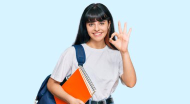 Genç İspanyol kız öğrenci çantası takıyor ve elinde kitap tutuyor. Parmaklarıyla imza atıyor, gülümsüyor. Mükemmel bir sembol. 