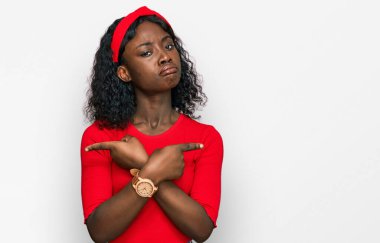 Gündelik giysiler giymiş güzel Afrikalı genç bir kadın her iki tarafı da parmaklarıyla işaret ediyor, farklı yönlere bakıyor. 