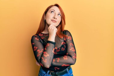 Güzel kızıl saçlı kadın gündelik giysiler giyiyordu. Kuşkuya yoğunlaşmıştı. Parmakları çenesinde ve yukarı bakıyordu. 