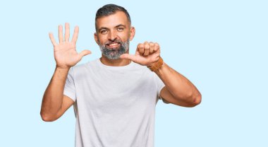 Orta yaşlı, beyaz tişört giyen yakışıklı bir adam altı numarayı gösterip işaret ederken kendinden emin ve mutlu bir şekilde gülümsüyor.. 