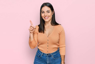 Genç İspanyol kadın gündelik kıyafetler giyip bir numarayı gösterip işaret ederken kendinden emin ve mutlu bir şekilde gülümsüyor.. 