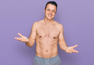 Mayo giyen yakışıklı genç adam. Neşeli gülümseyen, dostça kollar açık. Hoş geldin, olumlu ve kendinden emin selamlar. 