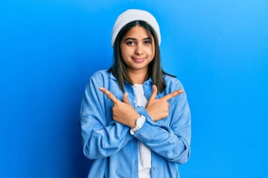 Her iki tarafı parmaklarıyla gösteren sevimli yün şapkalı genç Latin kadın farklı yönlere bakıyor. 