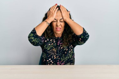 Masada oturan orta yaşlı, güzel bir kadın ağrı ve migrenden dolayı çaresiz ve stresli bir şekilde baş ağrısı çekiyor. Eller başının üstünde.. 
