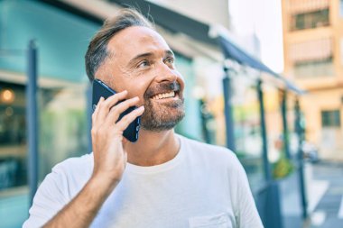 Orta yaşlı yakışıklı adam şehirde akıllı telefon kullanarak mutlu gülümsüyor..